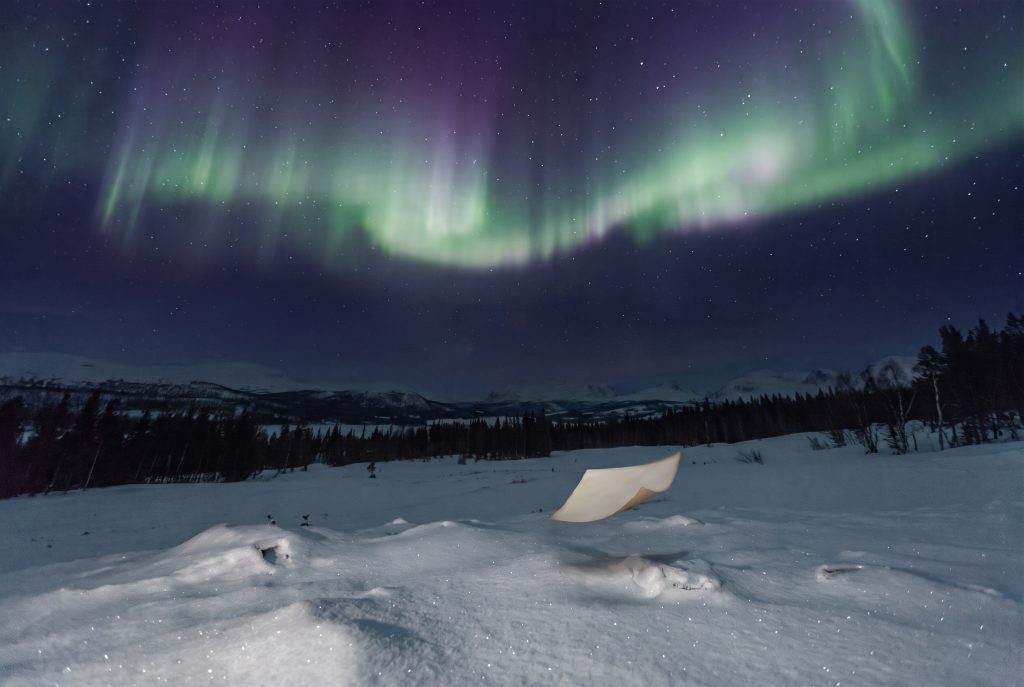 KI-generert bilde av papirark som svever mot nordlyset over et snødekket vinterlandskap
